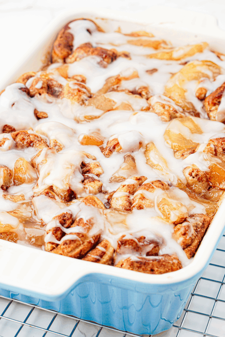A blue baking dish filled with apple cinnamon rolls topped with white icing, fresh out of the oven and resting on a cooling rack.