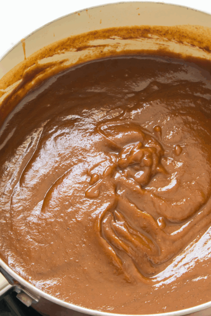 A pot filled with thick, smooth brown pumpkin butter being stirred, with the sweet sauce coating the sides of the pot.