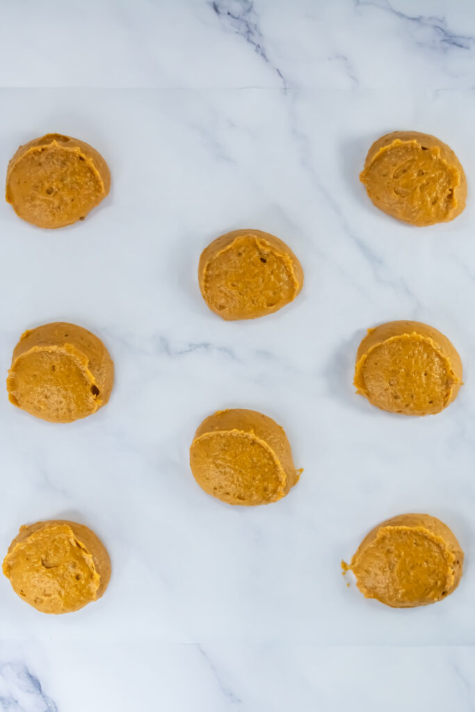 Eight unbaked cookie dough scoops spaced evenly on a white marble surface, ready for baking.