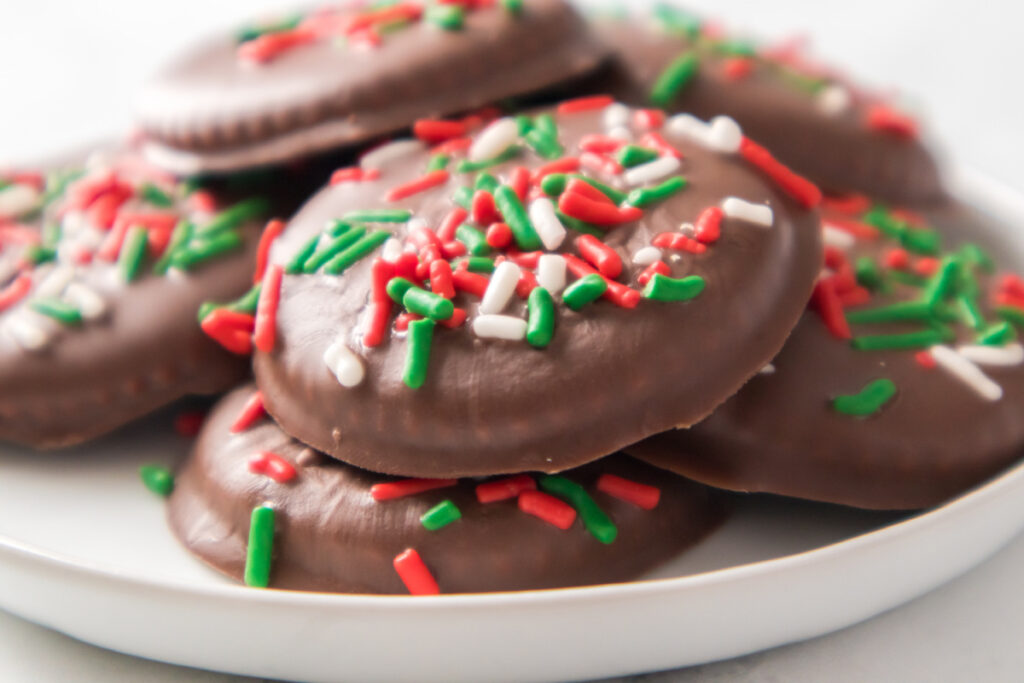 A plate of chocolate-covered cookies topped with red, green, and white sprinkles.