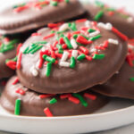 A plate of chocolate-covered cookies topped with red, green, and white sprinkles.