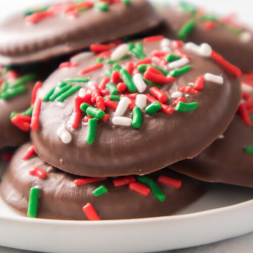 A plate of chocolate-covered cookies topped with red, green, and white sprinkles.
