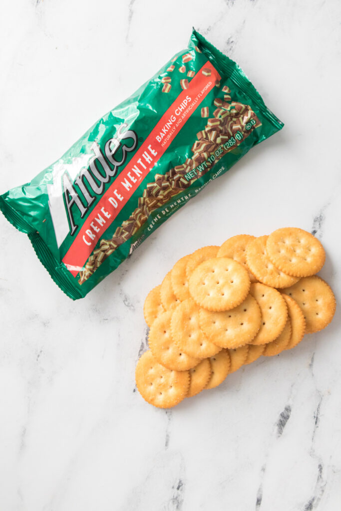 A package of Andes crème de menthe baking chips next to a stack of round, golden crackers on a white marble surface.
