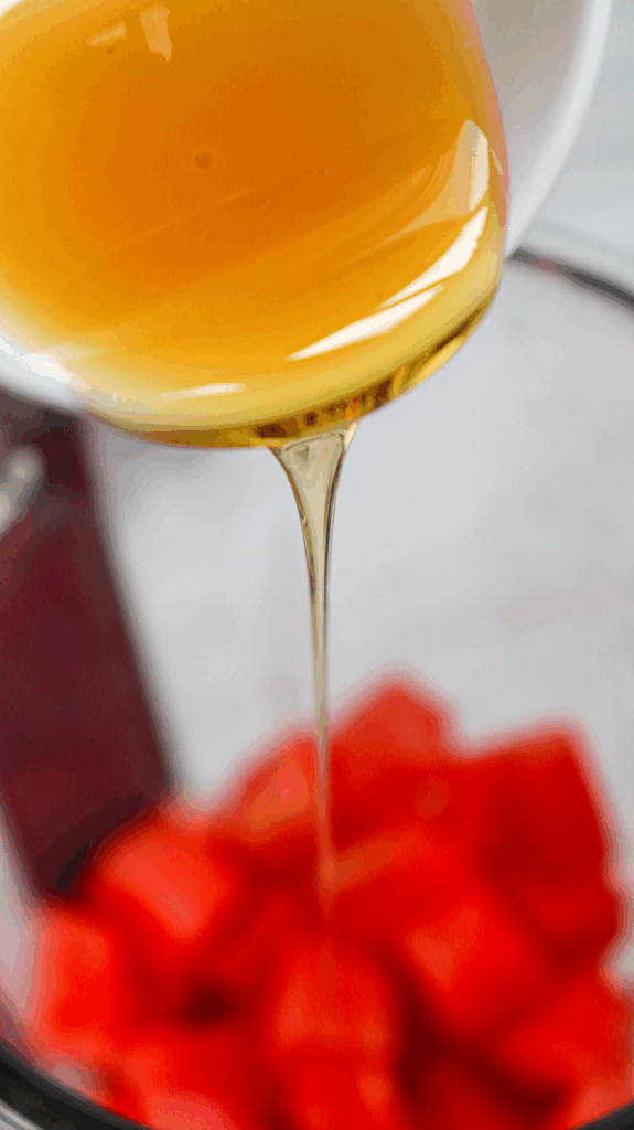 Honey being poured from a bowl onto a glass bowl filled with cubed watermelon pieces, perfect for creating a refreshing watermelon slushie.