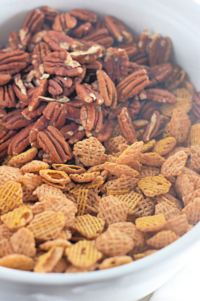 A white bowl filled with whole pecans on one side and square-shaped cereal pieces on the other side.