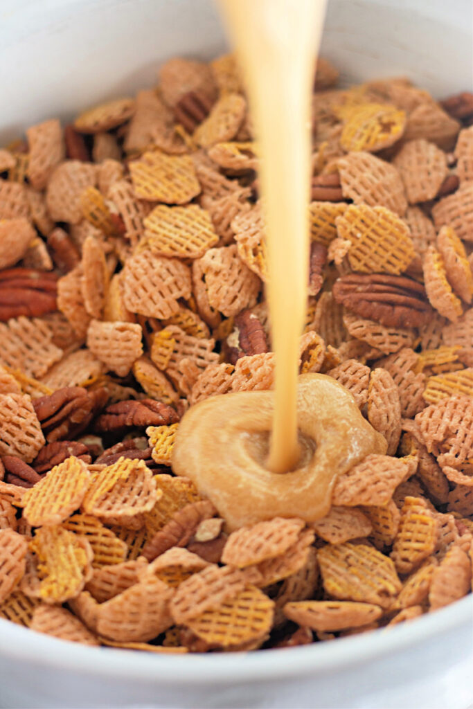 A creamy liquid is being poured over a bowl of mixed cereal and nuts.