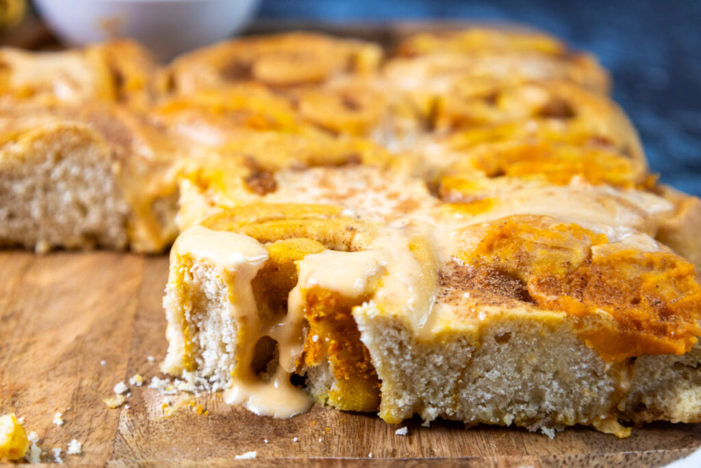 Close-up of freshly baked pumpkin cinnamon rolls with icing melting over the top, placed on a wooden surface.