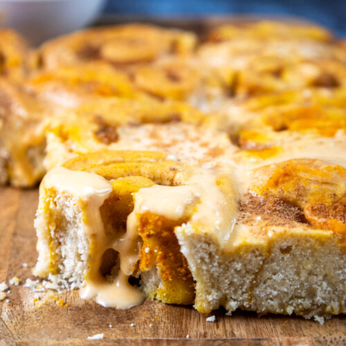 Close-up of freshly baked pumpkin cinnamon rolls with icing melting over the top, placed on a wooden surface.
