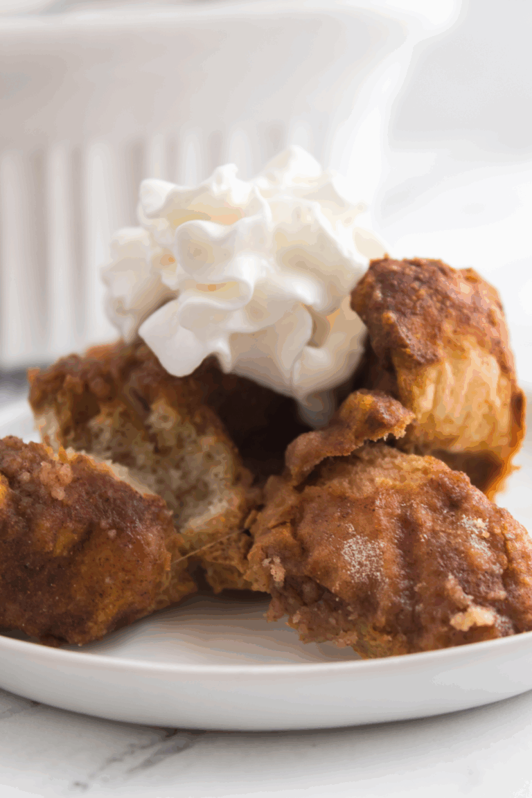 Four pieces of pumpkin French toast bake are stacked on a plate with a dollop of whipped cream on top; a white dish is in the background.