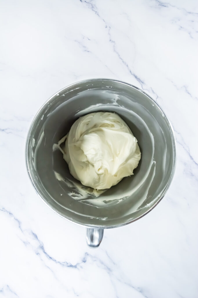 A metal mixing bowl containing a smooth, creamy white mixture, placed on a white marble surface.