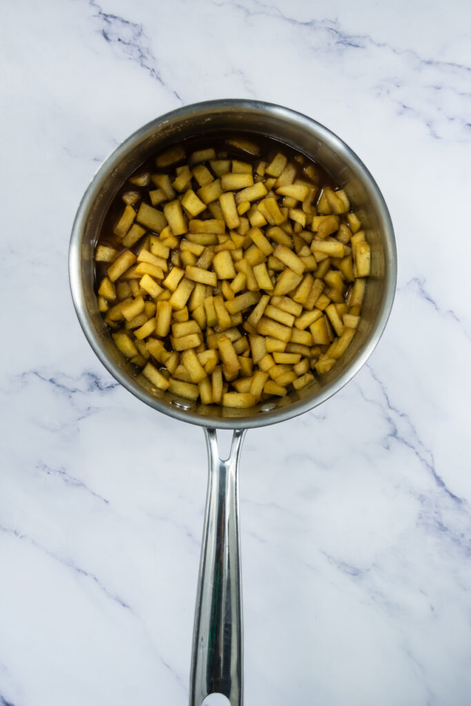 A saucepan filled with diced apples in liquid, placed on a white marble surface.
