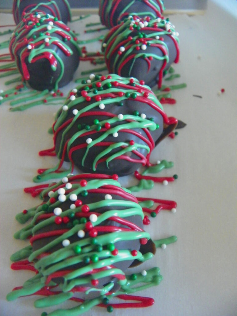 Chocolate-covered treats drizzled with red, green, and white icing, topped with red, green, and white sprinkles, arranged on a sheet of parchment paper.