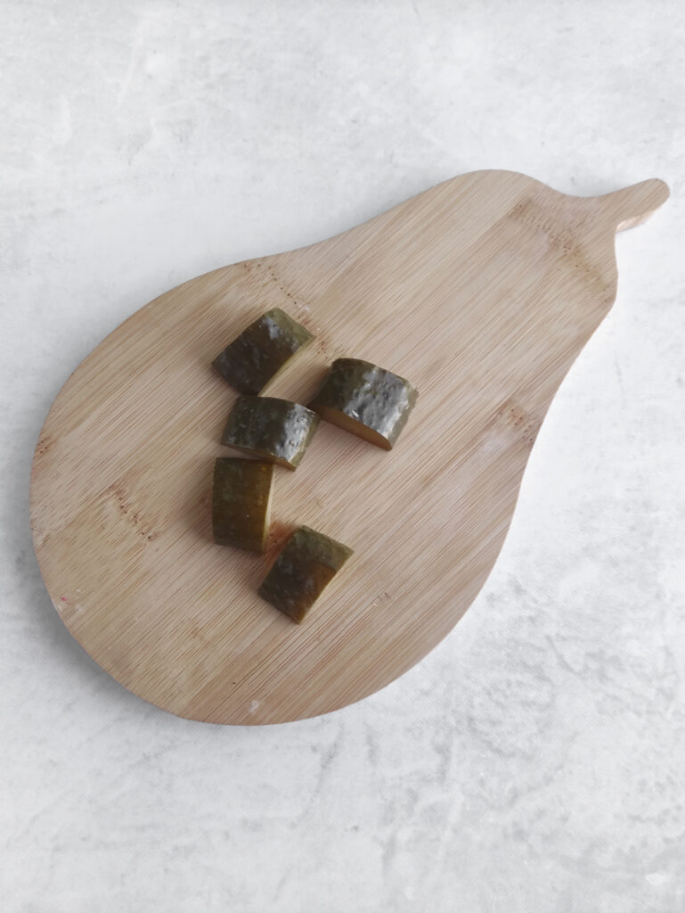 Five cucumber slices on a pear-shaped wooden cutting board placed on a light-colored surface.