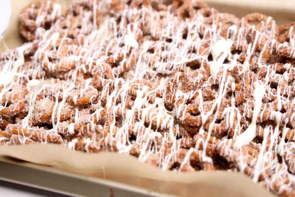 A tray of cinnamon sugar pretzels drizzled with white icing, arranged on parchment paper.