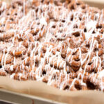 A tray of cinnamon sugar pretzels drizzled with white icing, arranged on parchment paper.