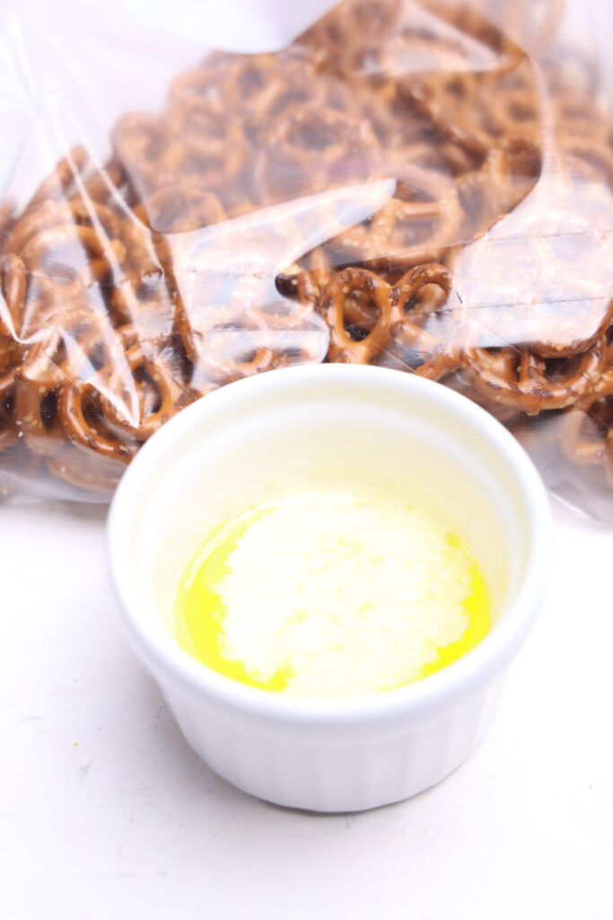 A small white ramekin with melted butter sits in front of a plastic bag filled with pretzels.
