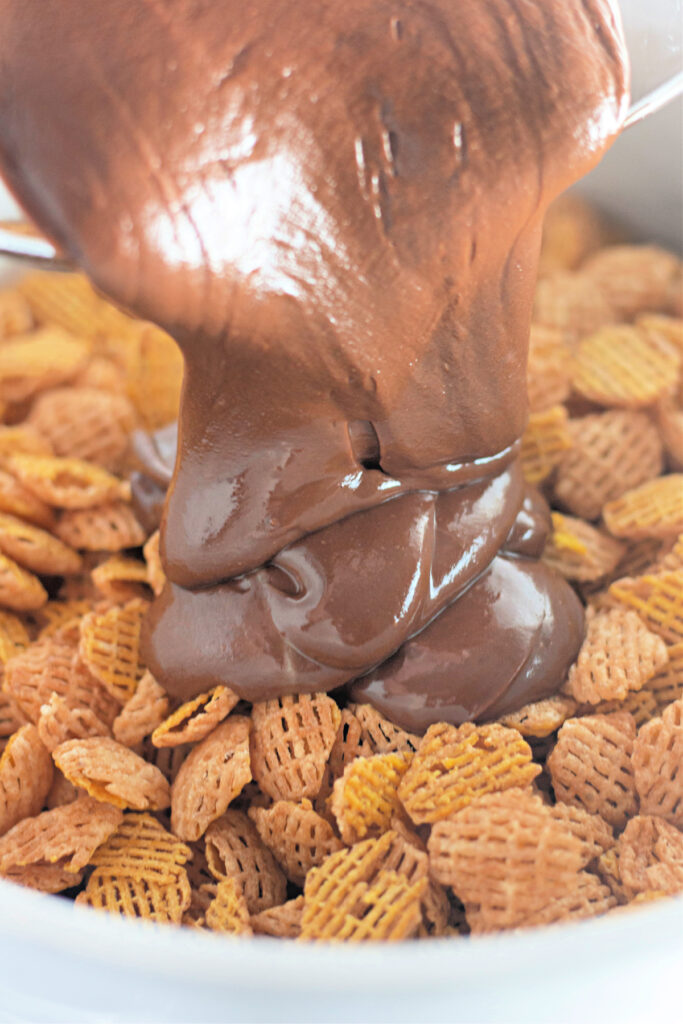 Chocolate mixture being poured over a bowl of square-shaped cereal pieces.
