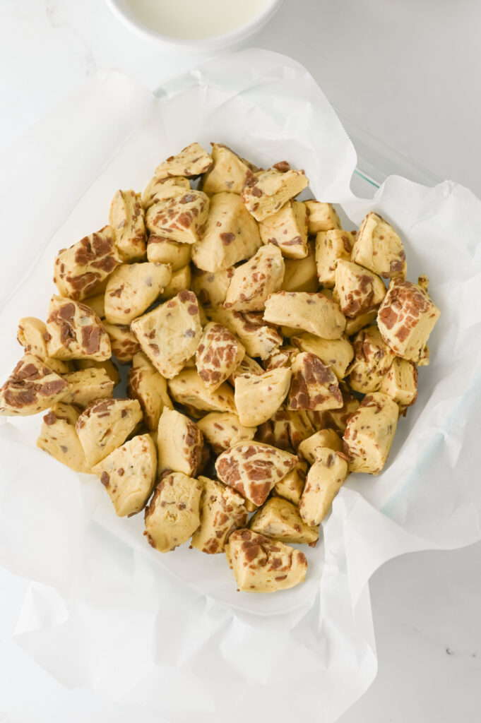 A bowl lined with parchment paper filled with golden brown, irregularly shaped baked snack pieces on a white surface.