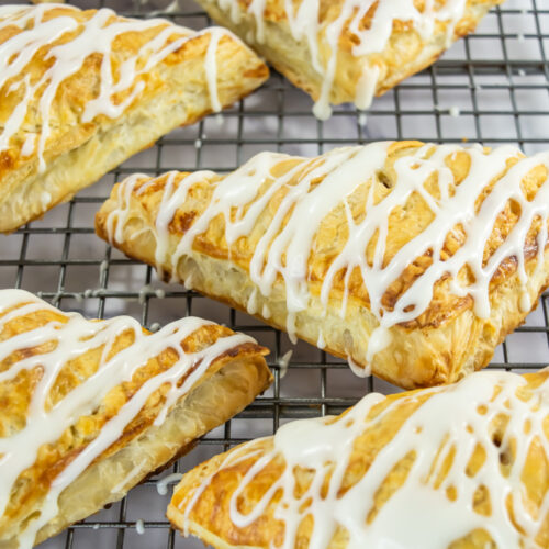 Six golden-brown, triangular pastries with white icing drizzle rest on a metal cooling rack.