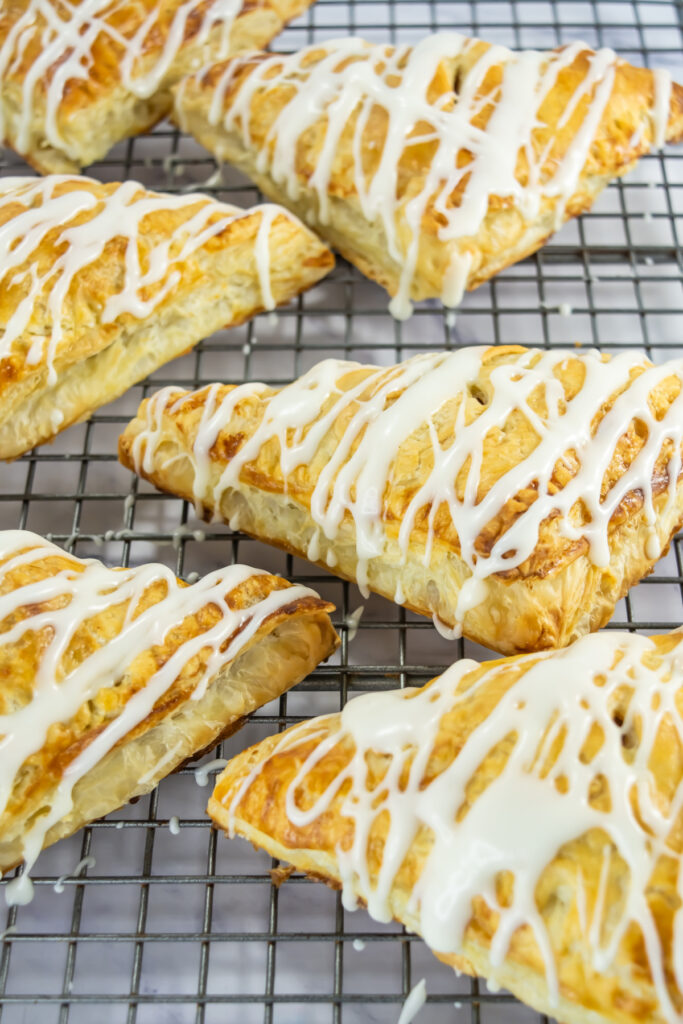 Six golden-brown, triangular pastries with white icing drizzle rest on a metal cooling rack.