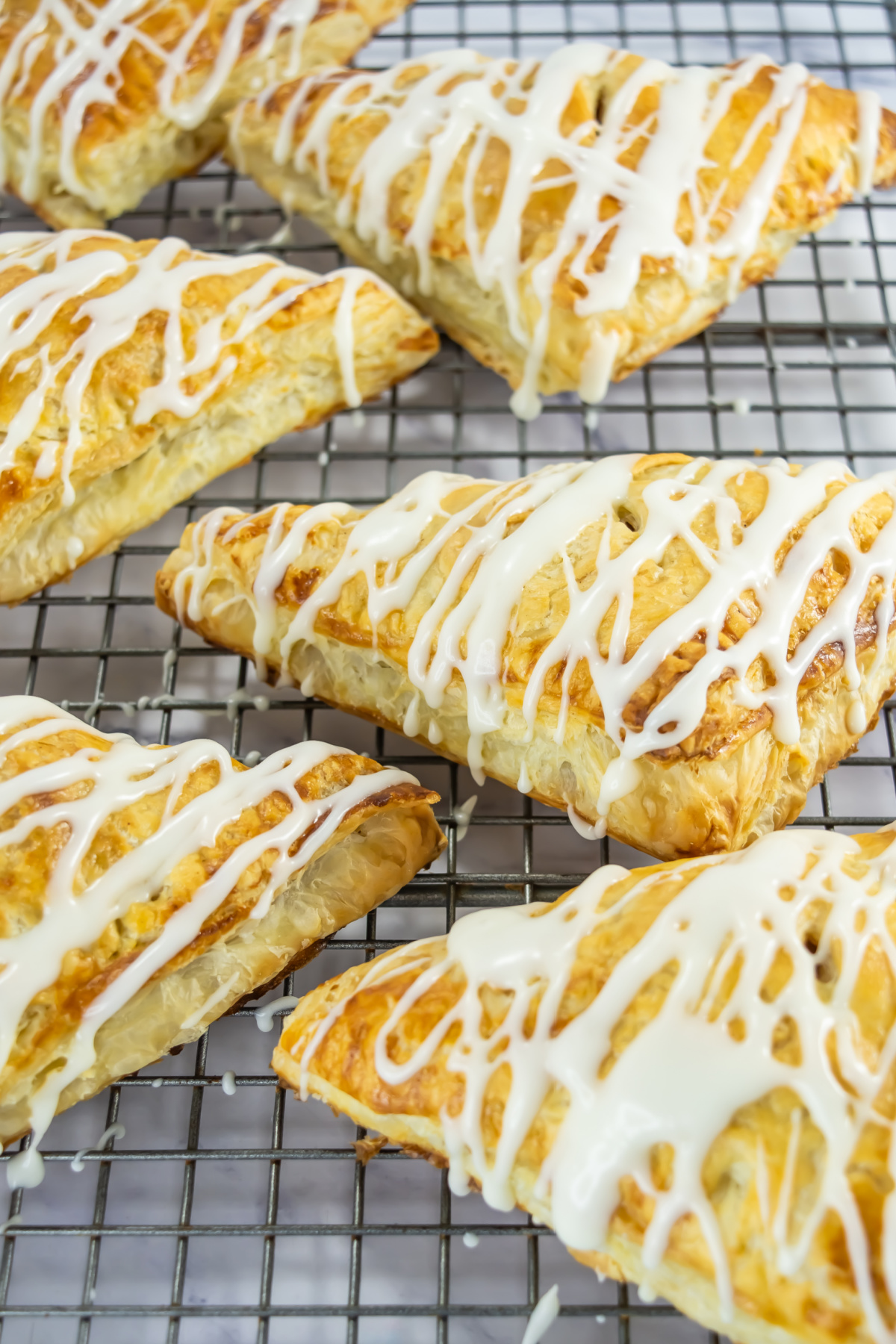 Six golden-brown, triangular pastries with white icing drizzle rest on a metal cooling rack.
