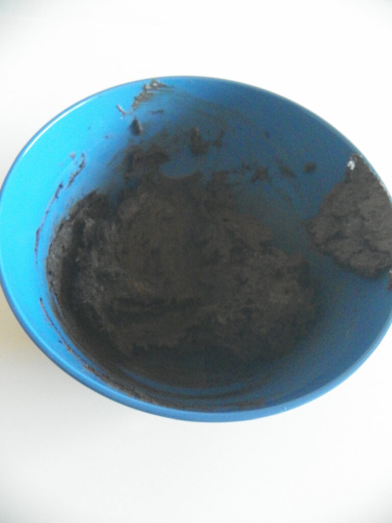 A blue bowl containing a dark, thick mixture with some residue on the sides, set against a white background.