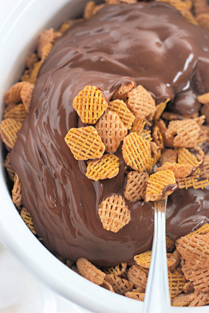 A bowl of wheat cereal squares with melted chocolate poured over them, with a metal spoon partially visible.
