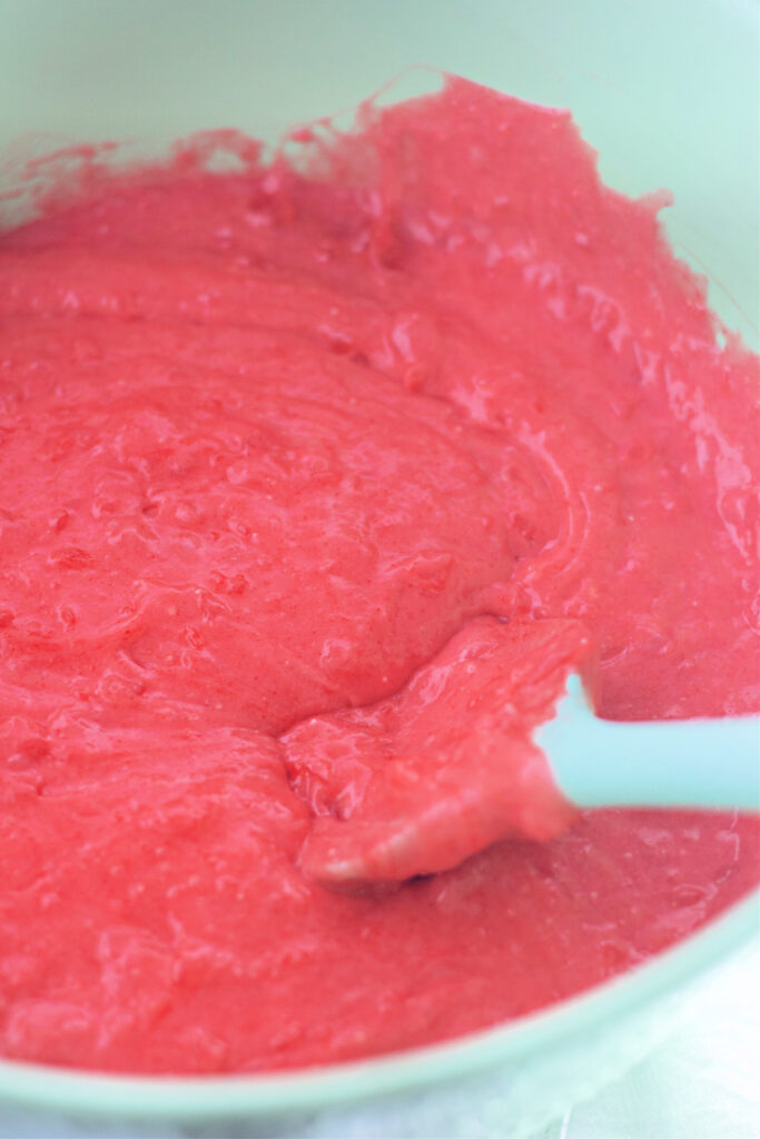 Bright pink cake batter being mixed in a white bowl with a white spatula.