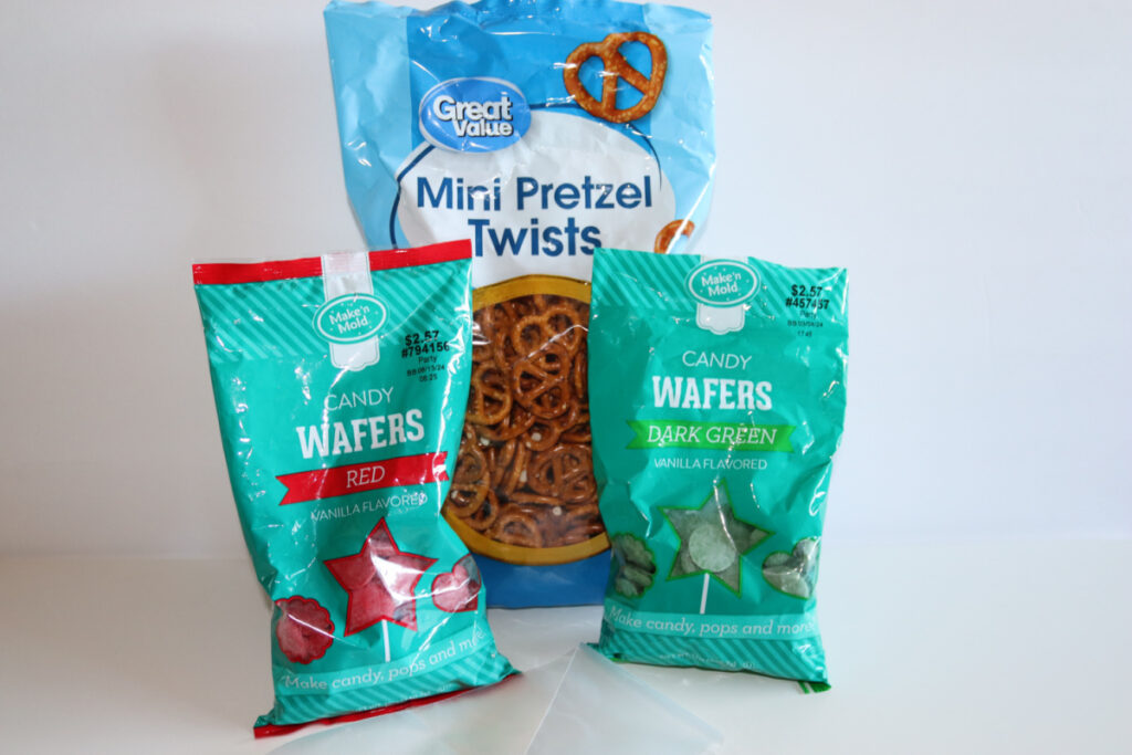 A bag of Great Value Mini Pretzel Twists behind two bags of Make'n Mold Candy Wafers in red and dark green flavors.