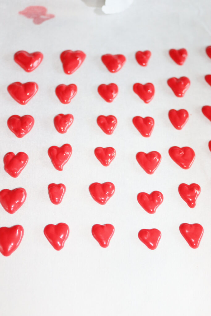 Rows of small red heart-shaped candies or decorations arranged on a white surface.