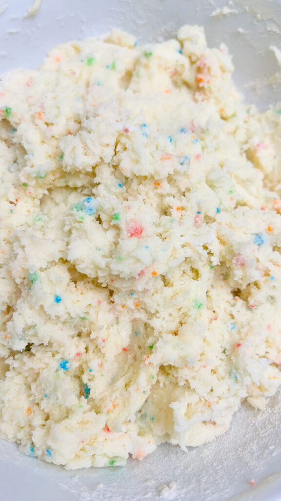 Cookie dough with colorful sprinkle bits mixed in, in a white bowl.