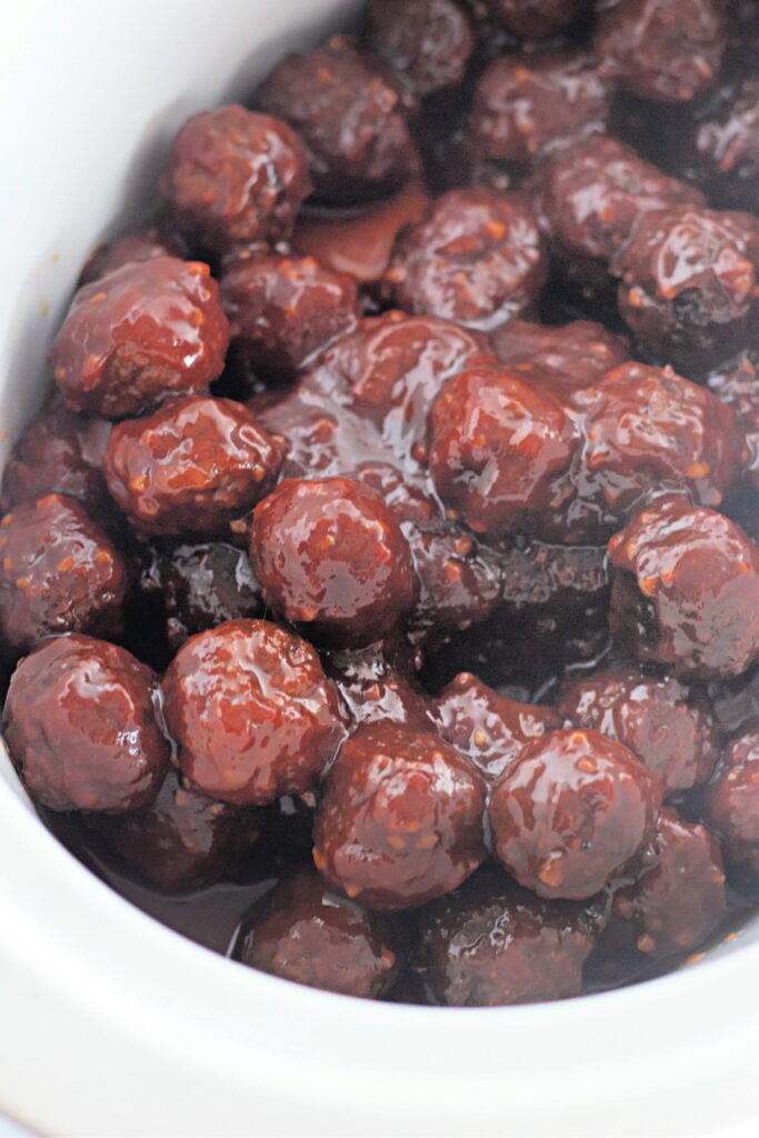 A close-up of meatballs coated in a thick, dark sauce inside a white slow cooker.