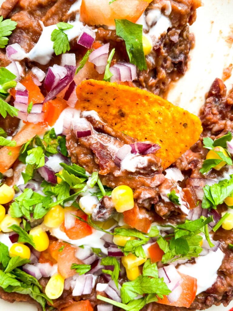 Close-up of a tortilla chip in a dip with beans, corn, tomato, red onion, cilantro, and sour cream.