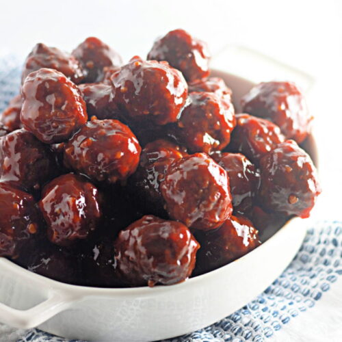 A white dish filled with glazed cocktail meatballs, set on a textured blue and white cloth.