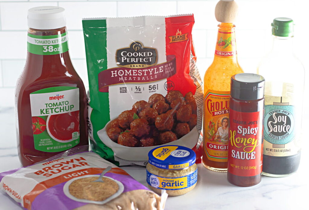 A variety of ingredients on a counter, including ketchup, frozen meatballs, hot sauce, soy sauce, brown sugar, honey sauce, and minced garlic.