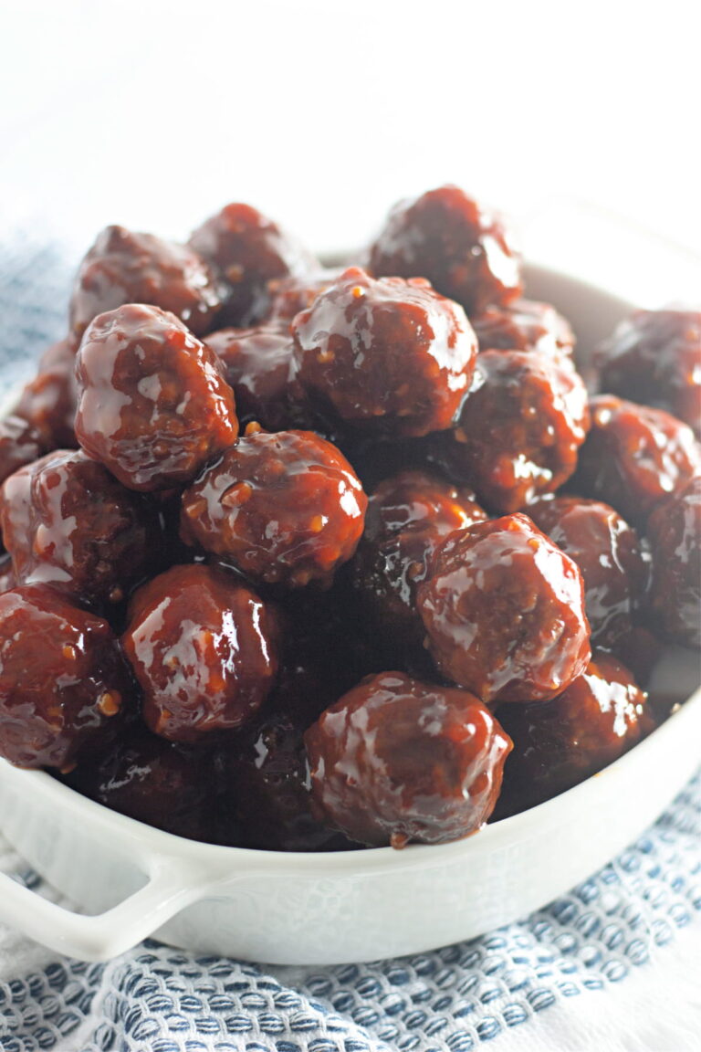 A white dish filled with glazed meatballs, piled high and coated in a shiny, dark sauce, resting on a blue and white patterned cloth.