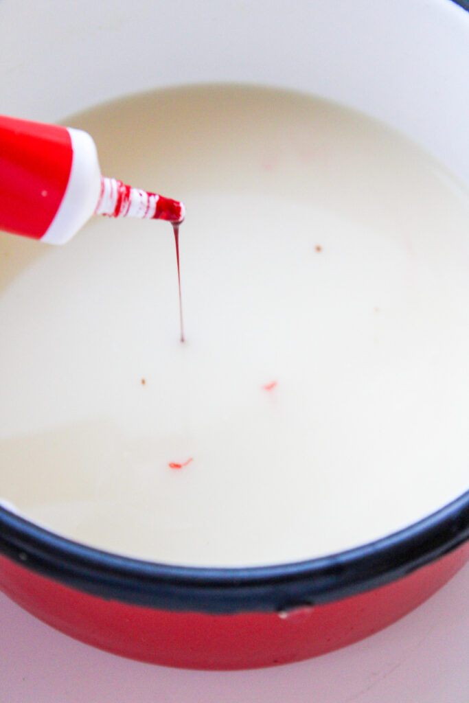 A red food coloring bottle drips liquid into a bowl of milk.