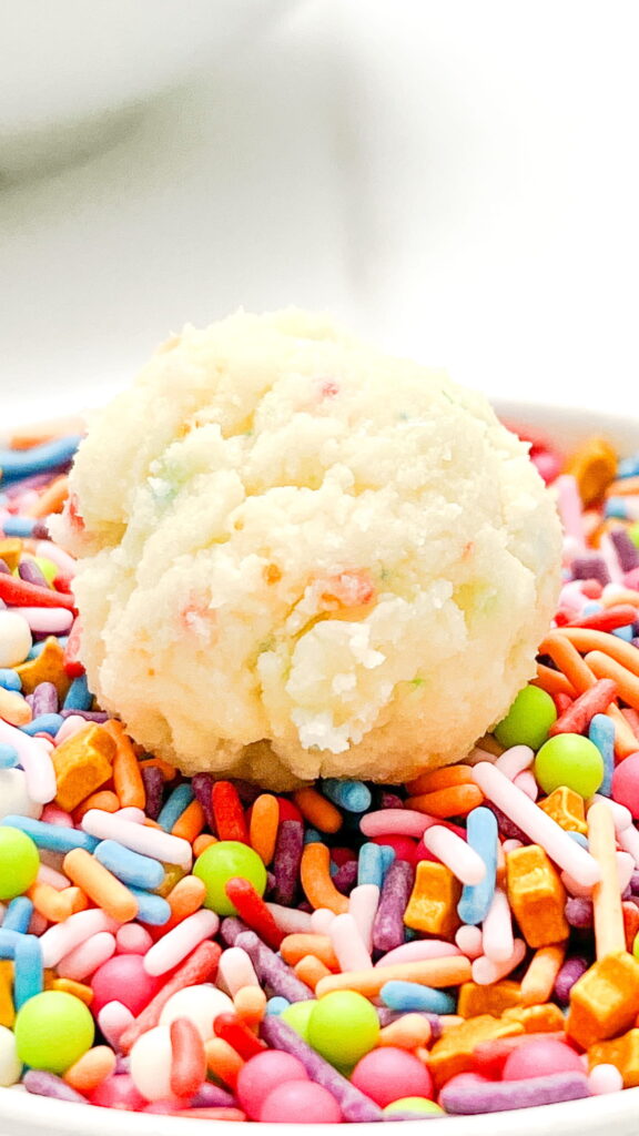 A scoop of cookie dough sits on a bed of colorful sprinkles.