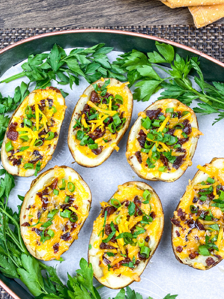 Six loaded potato skins topped with melted cheese, bacon bits, and chopped green onions, arranged on a tray garnished with fresh parsley.