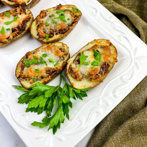 Three twice-baked potato halves topped with melted cheese and herbs are arranged on a white plate, garnished with fresh parsley. A green cloth lies beside the plate.