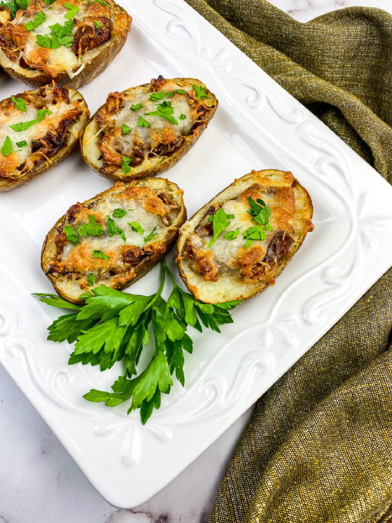 Three twice-baked potato halves topped with melted cheese and herbs are arranged on a white plate, garnished with fresh parsley. A green cloth lies beside the plate.