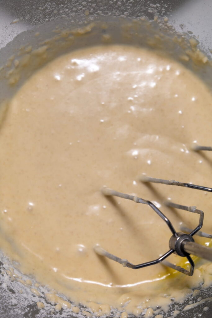A close-up view of cake batter being mixed in a bowl with an electric hand mixer.